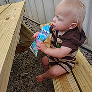 Everett is registered to the contest to win money with this photo: baby, barefoot, blond_hair, child, daylight, drinking, face, gravel, hands, happy, juice_pouch, outdoor, portrait, profile, sitting, snack, striped_clothing, toddler, wood, wooden_bench