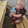 baby, barefoot, blond_hair, child, daylight, drinking, face, gravel, hands, happy, juice_pouch, outdoor, portrait, profile, sitting, snack, striped_clothing, toddler, wood, wooden_bench