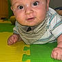 baby, infant, child, play_mat, indoor, curious, face, hands, striped_clothing, bib, expression, floor, colorful, play_area, person, portrait, closeup, skin, eyes, head