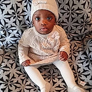 Essence joined the competition — help win amazing prizes! baby, child, infant, knit_hat, pom_pom, knit_sweater, white_tights, patterned_blanket, sitting, curious_look, indoors, cozy_clothing, cute, portrait, young_child, warm_clothes, hands, feet, face, expression