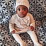 baby, child, infant, knit_hat, pom_pom, knit_sweater, white_tights, patterned_blanket, sitting, curious_look, indoors, cozy_clothing, cute, portrait, young_child, warm_clothes, hands, feet, face, expression