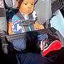 baby, car_seat, child, infant, seatbelt, clothing, sneakers, footwear, curly_hair, sunlight, shadow, sitting, indoor, safety, cute, person, young_child, black_hair, casual_wear, portrait