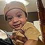 Rowen is registered to the contest to win money with this photo: baby, child, smiling, beanie, yellow_clothing, indoor, person, hand, wooden_post, ceiling_fan, portrait, happy, face, closeup, toddler, holding, casual, room, infant, cute