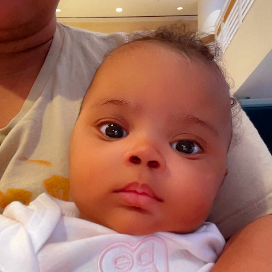 Daniah King joined the competition — help win amazing prizes! adult, arm, baby, candid, casual, child, close_up, curly_hair, expressionless, face, headwear, holding, indoor, light, modern_interior, person, portrait, selfie, skin, white_clothing