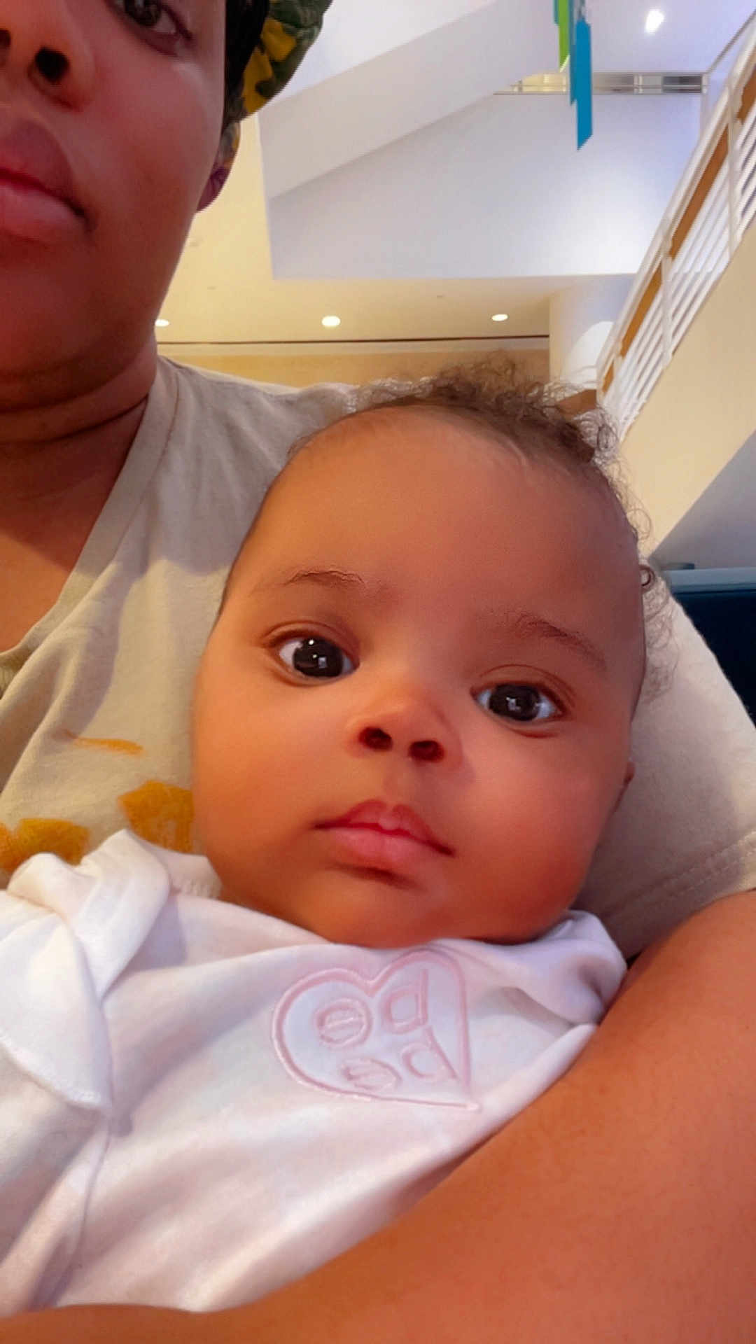 Daniah King joined the competition — help win amazing prizes! baby, adult, indoor, selfie, person, face, curly_hair, white_clothing, holding, close_up, expressionless, headwear, skin, light, modern_interior, arm, child, candid, portrait, casual