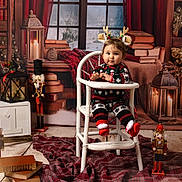 Olivia a rejoint le concours — aidez-le/la à gagner de superbes lots ! baby, child, high_chair, holiday_pajamas, reindeer_antlers, nutcracker, candle, books, blanket, plaid, festive, christmas, decorations, window, wood_floor, lantern, indoor, portrait, cute, smiling