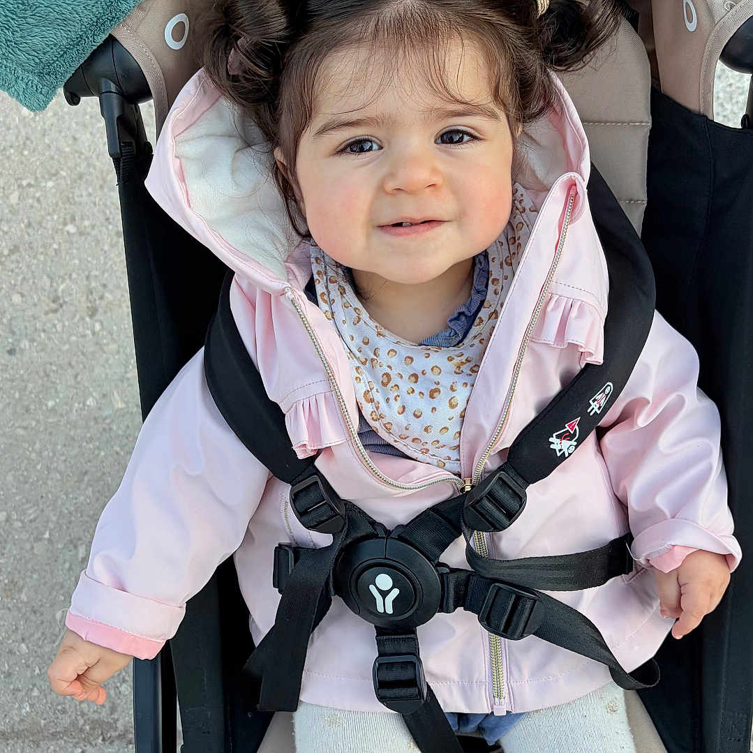 éline a rejoint le concours — aidez-le/la à gagner de superbes lots ! child, toddler, stroller, pink_jacket, white_tights, smiling, hair_tied, outdoor, baby, cute, seatbelt, person, face, clothing, baby_stroller, small_child, casual, happy, young, portrait