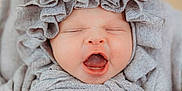 Olenna is registered to the contest to win money with this photo: apparel, baby, bonnet, child, closeup, clothing, cute, fabric, face, headwear, indoors, infant, neutral_background, newborn, person, portrait, sleepy, soft, texture, yawning