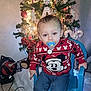 child, toddler, pacifier, christmas_tree, christmas, sweater, mickey_mouse, blue_chair, decorations, lights, ornament, candy_cane, jeans, sneakers, indoor, holiday, sitting, face, smile, plastic_chair