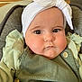 baby, child, face, headband, bow, green_clothing, ruffles, cushioned_seat, indoors, portrait, cute, chubby_cheeks, serious_expression, infant, button, fabric, person, closeup, headwear, young_child