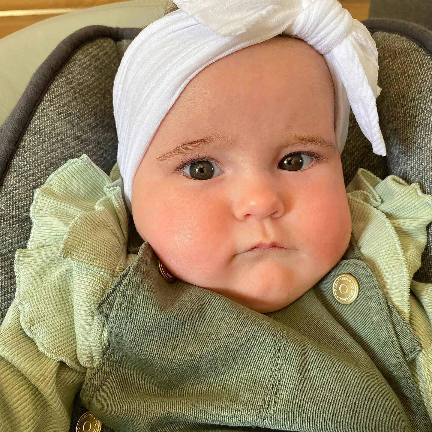 Luna participe au concours pour gagner de l'argent avec cette photo : baby, bow, button, child, chubby_cheeks, closeup, cushioned_seat, cute, fabric, face, green_clothing, headband, headwear, indoors, infant, person, portrait, ruffles, serious_expression, young_child