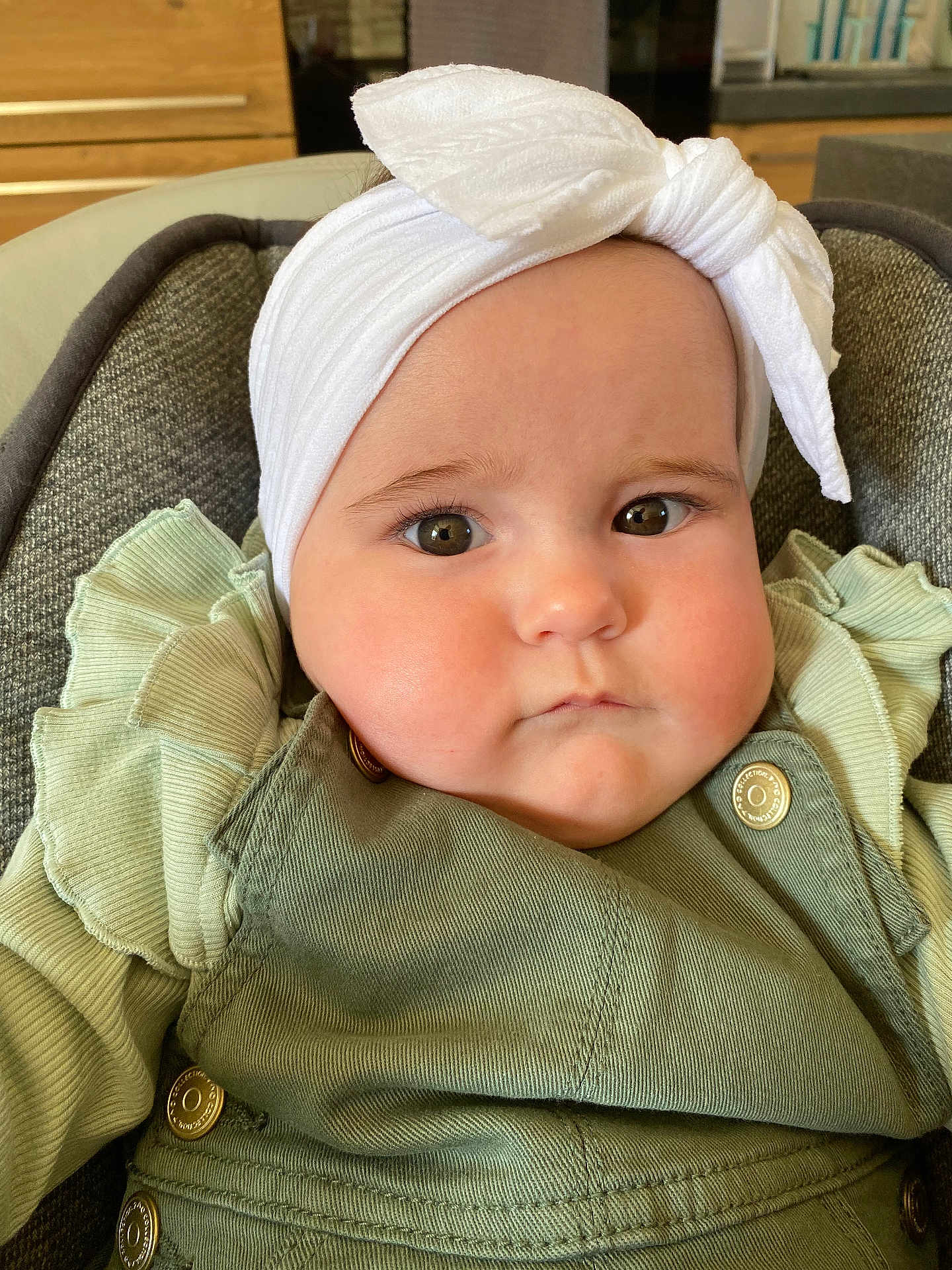 Luna participe au concours pour gagner de l'argent avec cette photo : baby, child, face, headband, bow, green_clothing, ruffles, cushioned_seat, indoors, portrait, cute, chubby_cheeks, serious_expression, infant, button, fabric, person, closeup, headwear, young_child