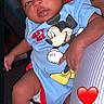 baby, infant, mickey_mouse, onesie, blue_clothing, white_socks, person, child, cute, resting, lap, heart_emoji, red_heart, indoor, portrait, smiling, young_child, skin, hand, face