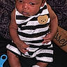 baby, infant, striped_clothing, socks, teddy_bear_patch, tattoo, person, child, sitting, indoors, black_background, cute, portrait, young, small, cozy, casual, clothing, hand, skin