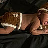 Emmanuel is registered to the contest to win money with this photo: baby, infant, knit_hat, knit_shorts, football_theme, lying_down, surprised_expression, dark_background, baby_booties, child, cute, newborn, portrait, soft_light, cozy, hand, face, mouth_open, clothing, sleepwear