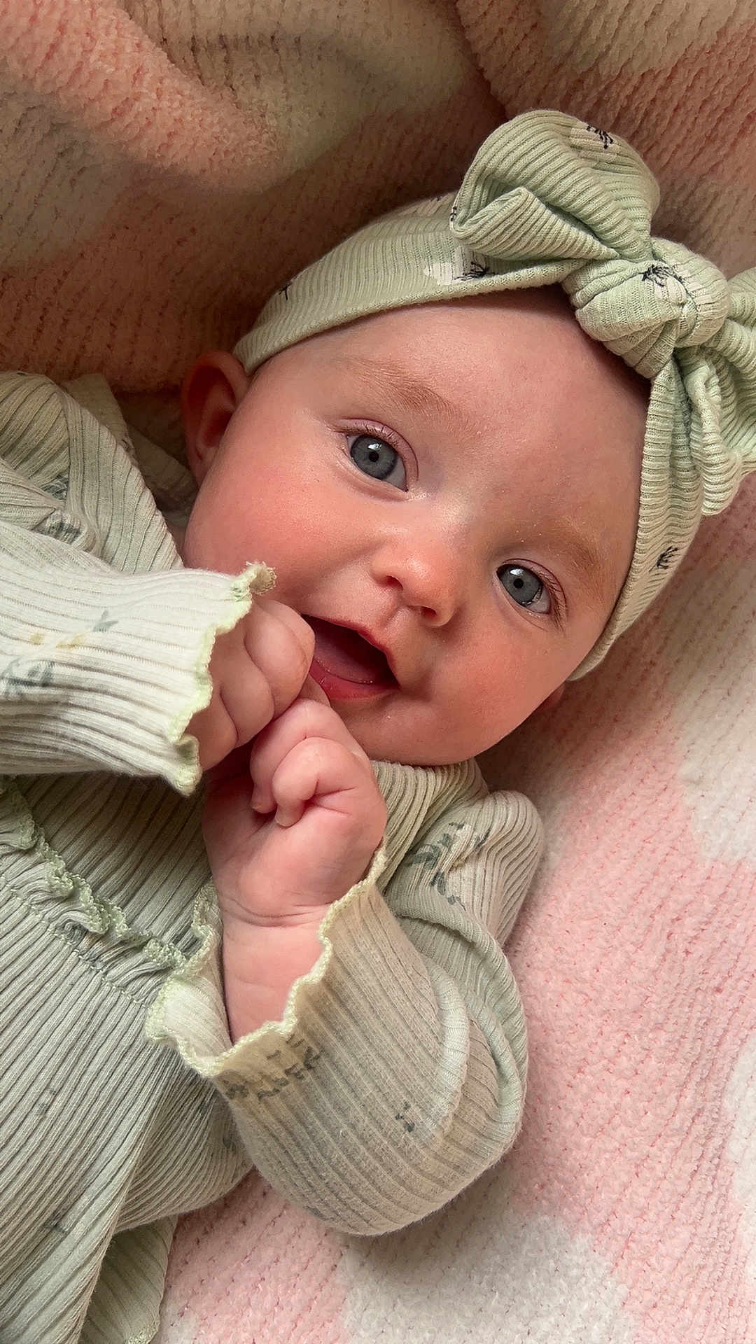 Lottie is registered to the contest to win money with this photo: baby, infant, child, headband, blue_eyes, smile, hands, clothing, ribbed_fabric, pink_blanket, close_up, portrait, cute, soft_texture, happy, lying_down, skin, face, indoor, cozy