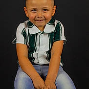 Wesley a rejoint le concours — aidez-le/la à gagner de superbes lots ! child, boy, portrait, smiling, studio, dark_background, striped_shirt, green_shirt, jeans, sitting, stool, short_hair, earring, hands_clasped, cute, playful_expression, one_person, photography, watermark, indoor