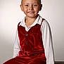 child, young_child, smiling, portrait, red_velvet, vest, white_shirt, sitting, studio_background, wooden_crate, short_hair, haircut, happy, cute, hands, buttons, pants, formal_outfit, pose, indoor