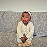 baby, child, infant, sitting, couch, gray_couch, knit_sweater, headband, bow, curious, indoors, portrait, cute, young_child, footwear, soft_lighting, wall, orange_heart_emoji, expression, cozy