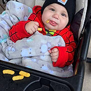 Malachi is registered to the contest to win money with this photo: baby, child, infant, stroller, beanie, red_outfit, blanket, snack, puffs, tongue_out, smiling, portrait, cozy, outdoor, seated, carriage, baby_clothing, playful, face, photography