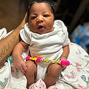 Khilani is registered to the contest to win money with this photo: newborn, baby, infant, white_onesie, pacifier_clip, beads, hand, tattoo, blanket, soft_focus, indoor, portrait, skin, cute, expression, holding, legs, pink, yellow, person