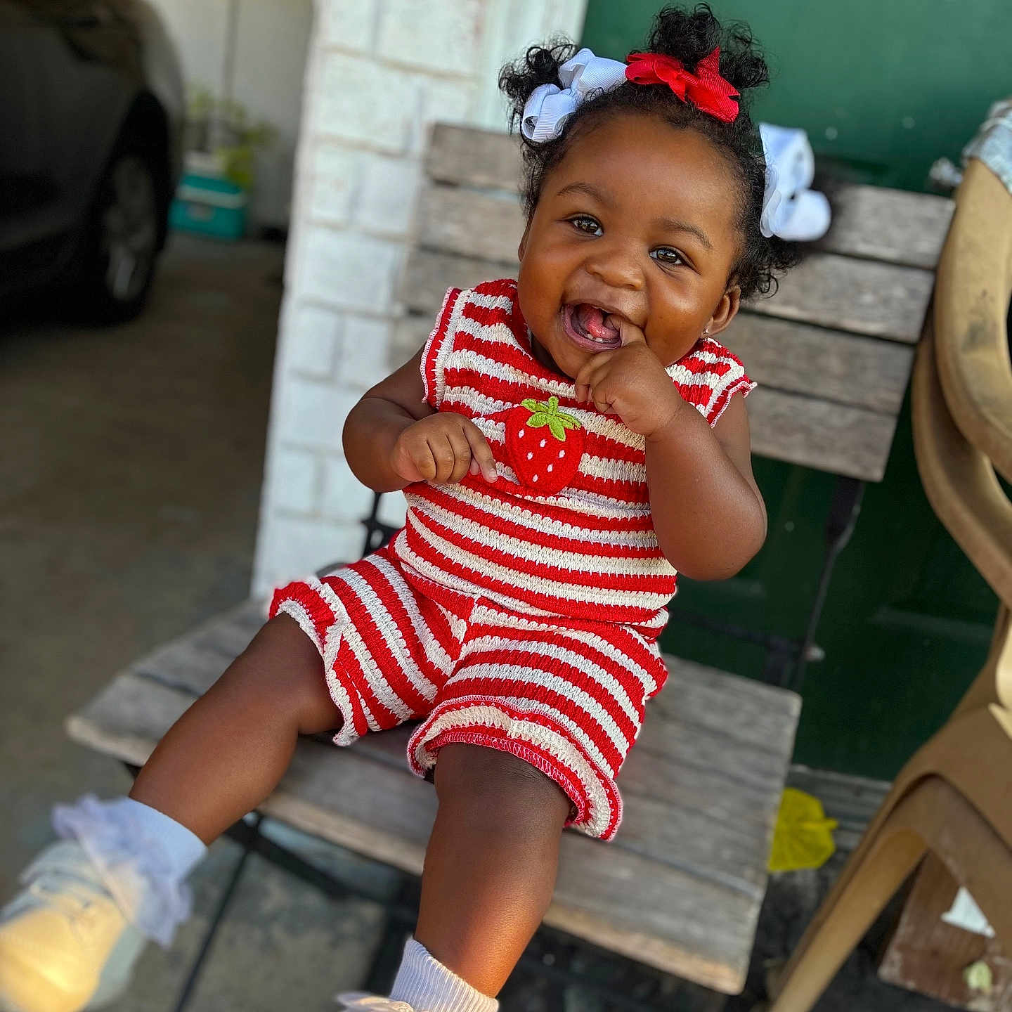 Khilani is registered to the contest to win money with this photo: baby, chair, child, clothing, cute, green_door, hair_bows, happy, outdoor, person, portrait, red, seat, shoes, smiling, socks, striped, toddler, white, wood