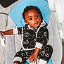 baby, infant, child, blue_cushion, baby_seat, black_outfit, cloud_pattern, striped_socks, floor, marble_floor, indoor, cute, wide_eyes, curious, sitting, hand, footwear, cozy, comfortable, person