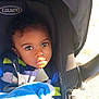 Kario is registered to the contest to win money with this photo: toddler, child, baby, stroller, graco, blanket, blue_blanket, striped_jacket, sunlight, outdoor, curious, wide_eyes, face, portrait, infant, seatbelt, baby_carrier, baby_seat, person, closeup