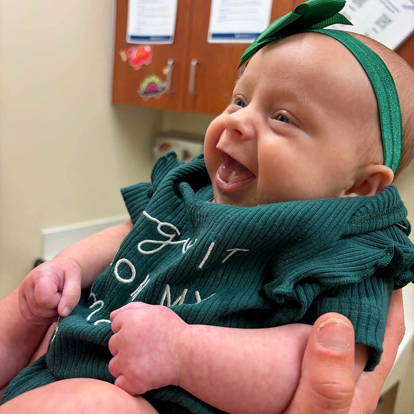 Laelyn Faith is registered to the contest to win money with this photo: baby, infant, smiling, green_headband, green_clothing, happy, hand, person, indoor, cabinet, wall, paper, document, holding, cute, skin, face, expression, young_child, human