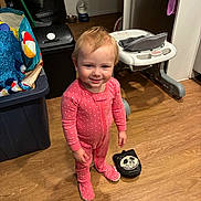 Emma'Mae joined the competition — help win amazing prizes! toddler, child, pink_onesie, polka_dot, smile, standing, wooden_floor, high_chair, toy, storage_bin, household, indoor, floor, person, face, footwear, curly_hair, baby, room, playful