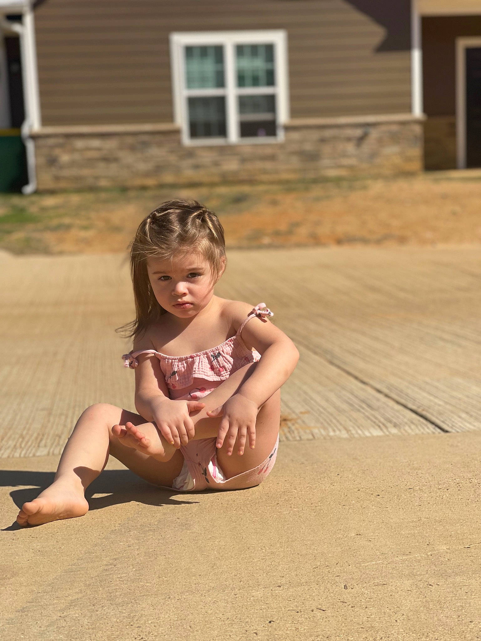 Ember is registered to the contest to win money with this photo: asphalt, barefoot, blond, floor, flooring, foot, fun, grass, happy, house, human_leg, knee, leisure, person, recreation, road_surface, sitting, thigh, toddler, window
