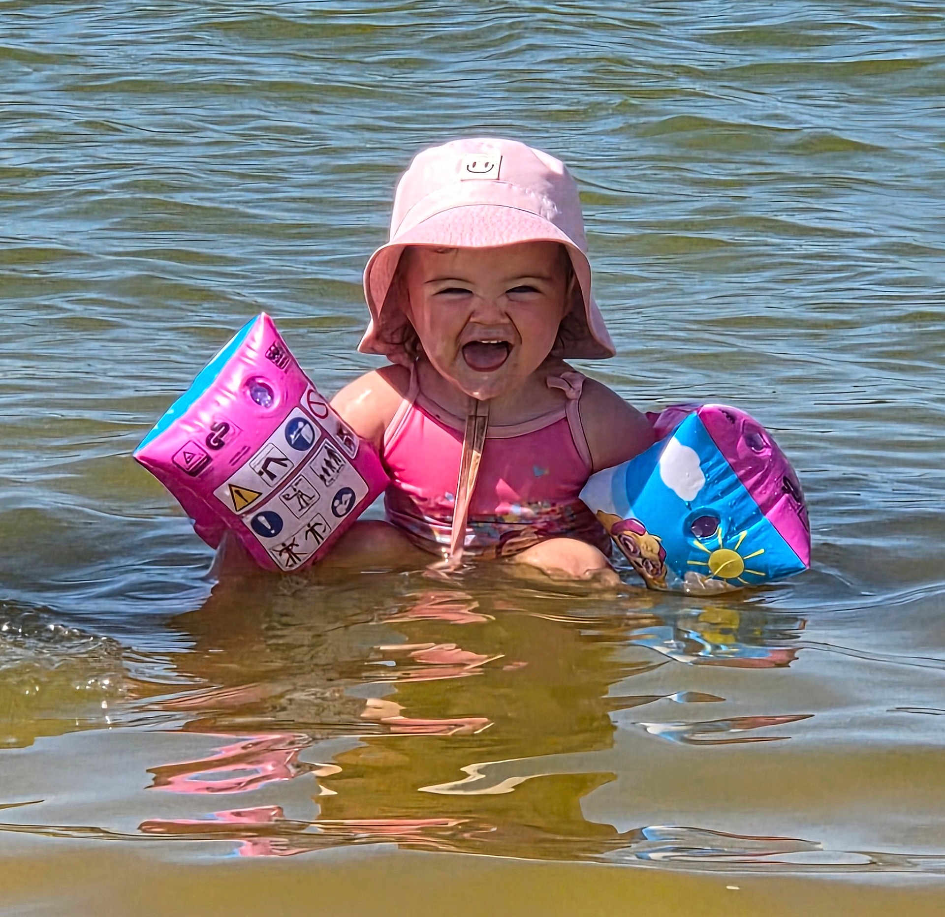 Alba a rejoint le concours — aidez-le/la à gagner de superbes lots ! toddler, child, water, floaties, pink_hat, pink_swimsuit, summer, lake, splashing, happy, smiling, sunny, outdoor, fun, playing, water_reflection, warm_weather, baby, swimming, daytime