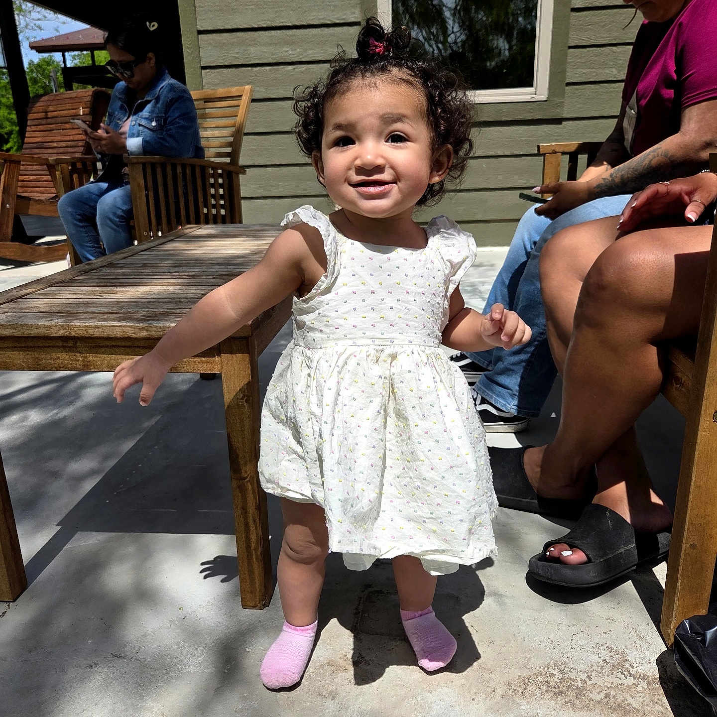 Eliana joined the competition — help win amazing prizes! adult, casual, child, concrete_floor, family, glasses, green_siding, happy, outdoor, patio, phone, pink_socks, portrait, shadow, smile, sunlight, toddler, white_dress, wooden_chair, wooden_table