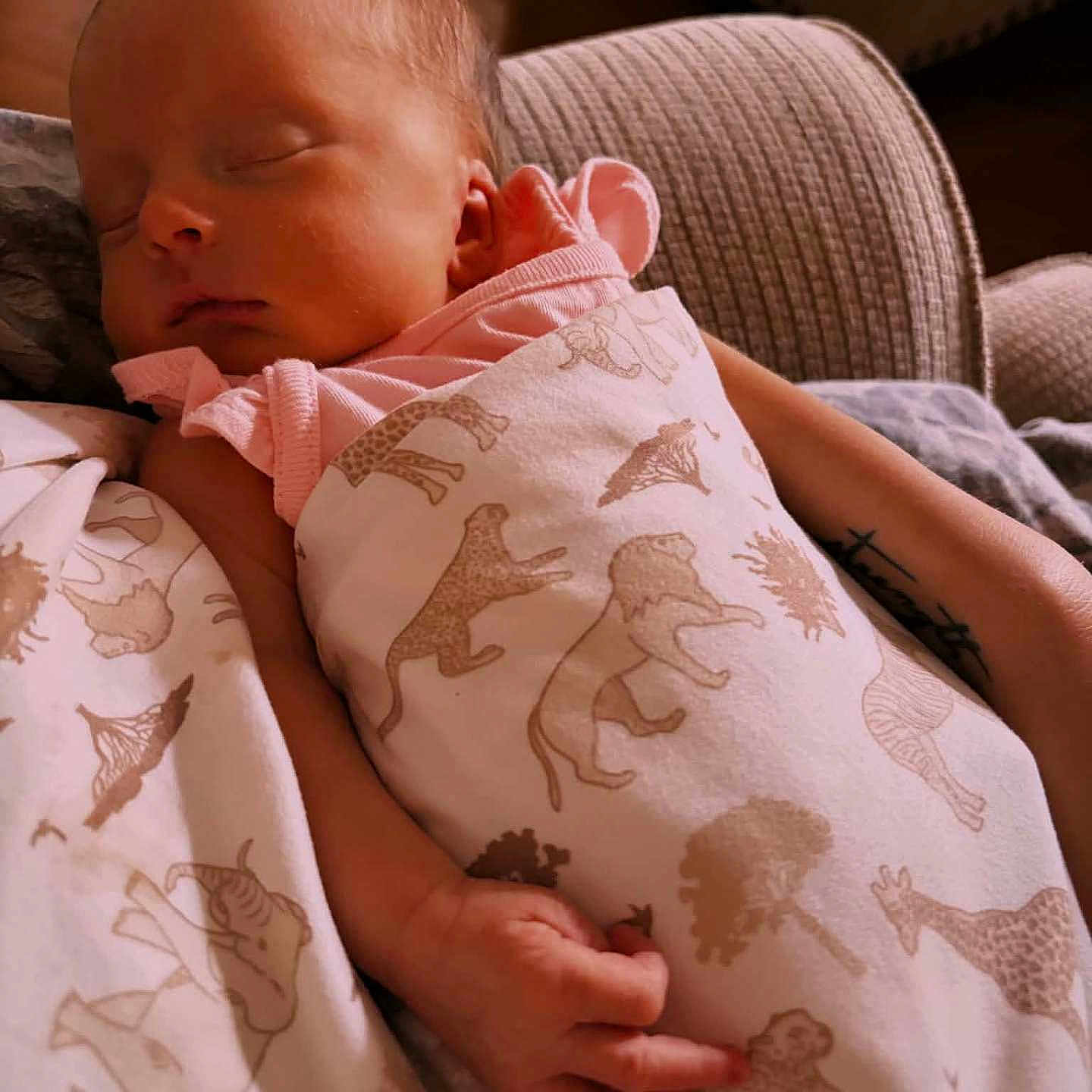 Naomi joined the competition — help win amazing prizes! baby, sleeping, blanket, animal_print, couch, arm, tattoo, indoor, cozy, soft_lighting, infant, peaceful, resting, child, person, wrapped, pink_clothing, hand, furniture, portrait