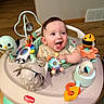 baby, child, smiling, happy, toy, activity_center, indoor, playtime, colorful, infant, face, hands, wooden_floor, cute, joyful, clothing, seat, plastic, entertainment, developmental_toys