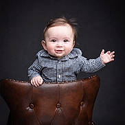 Ryder joined the competition — help win amazing prizes! baby, child, smiling, waving, leather_chair, portrait, studio, cute, happy, black_background, button_up_shirt, plaid, young_child, face, head, person, furniture, sitting, expression, small_hand