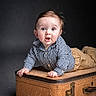 baby, child, vintage_suitcase, blue_shirt, tan_pants, curious_expression, studio_lighting, portrait, indoor, infant, hands, face, eyes, mouth_open, clothing, cute, young, person, background, posing