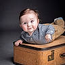 baby, child, smiling, face, portrait, vintage_suitcase, checkered_shirt, khaki_pants, lying_down, studio, indoor, cute, young, person, fashion, happy, expression, human, background, soft_lighting