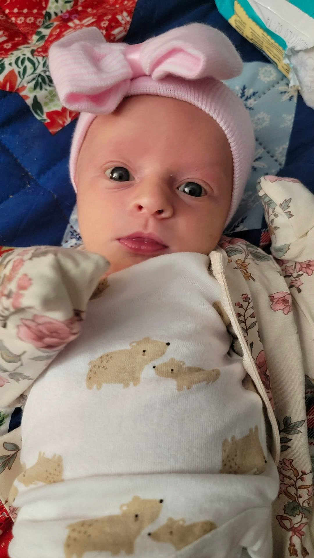 Berkeley is registered to the contest to win money with this photo: baby, infant, pink_bow, hat, onesie, bear_pattern, quilt, blanket, floral, clothing, face, eyes, cute, newborn, portrait, lying_down, headwear, baby_clothes, closeup, child