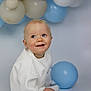 baby, child, smiling, balloons, blue, cream, white_clothing, sitting, cute, portrait, happy, indoor, infant, soft_lighting, background_blur, playful, young_child, head, face, person