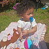 toddler, child, pacifier, curly_hair, blanket, plush_toy, outdoor, grass, flower_bush, sunlight, toy, colorful_leggings, garden, young_child, cute, sitting, playtime, soft_texture, summer, casual_clothing