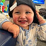 Santino is registered to the contest to win money with this photo: baby, child, smiling, cap, backwards_cap, onesie, mickey_mouse, indoor, toy, television, couch, carpet, hand, face, cheeks, tongue, happy, cute, clothing, person