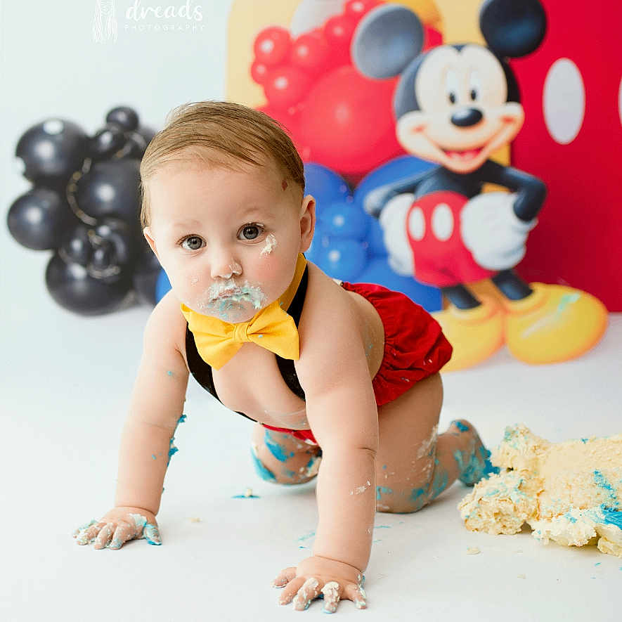 Santino is registered to the contest to win money with this photo: baby, balloons, birthday, blue_icing, cake, celebration, child, crawling, cute, face_paint, fun, indoor, messy, mickey_mouse, party, photography, red_shorts, smash_cake, white_floor, yellow_bowtie