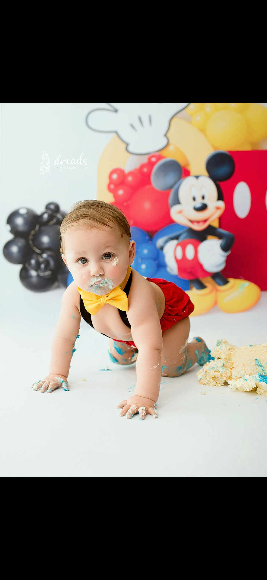 Santino is registered to the contest to win money with this photo: baby, child, mickey_mouse, balloons, cake, smash_cake, messy, crawling, yellow_bowtie, red_shorts, blue_icing, white_floor, birthday, celebration, party, cute, face_paint, photography, indoor, fun