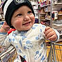 toddler, child, baby, shopping_cart, beanie, hat, clothing, mickey_mouse, onesie, store, indoor, shelf, products, smiling, happy, face, hand, seatbelt, retail, shopping