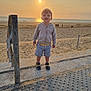 toddler, child, beach, sunset, sand, sea, ocean, clothing, hoodie, shorts, sandals, concrete, railing, outdoor, sky, sun, people, shadows, summer, vacation