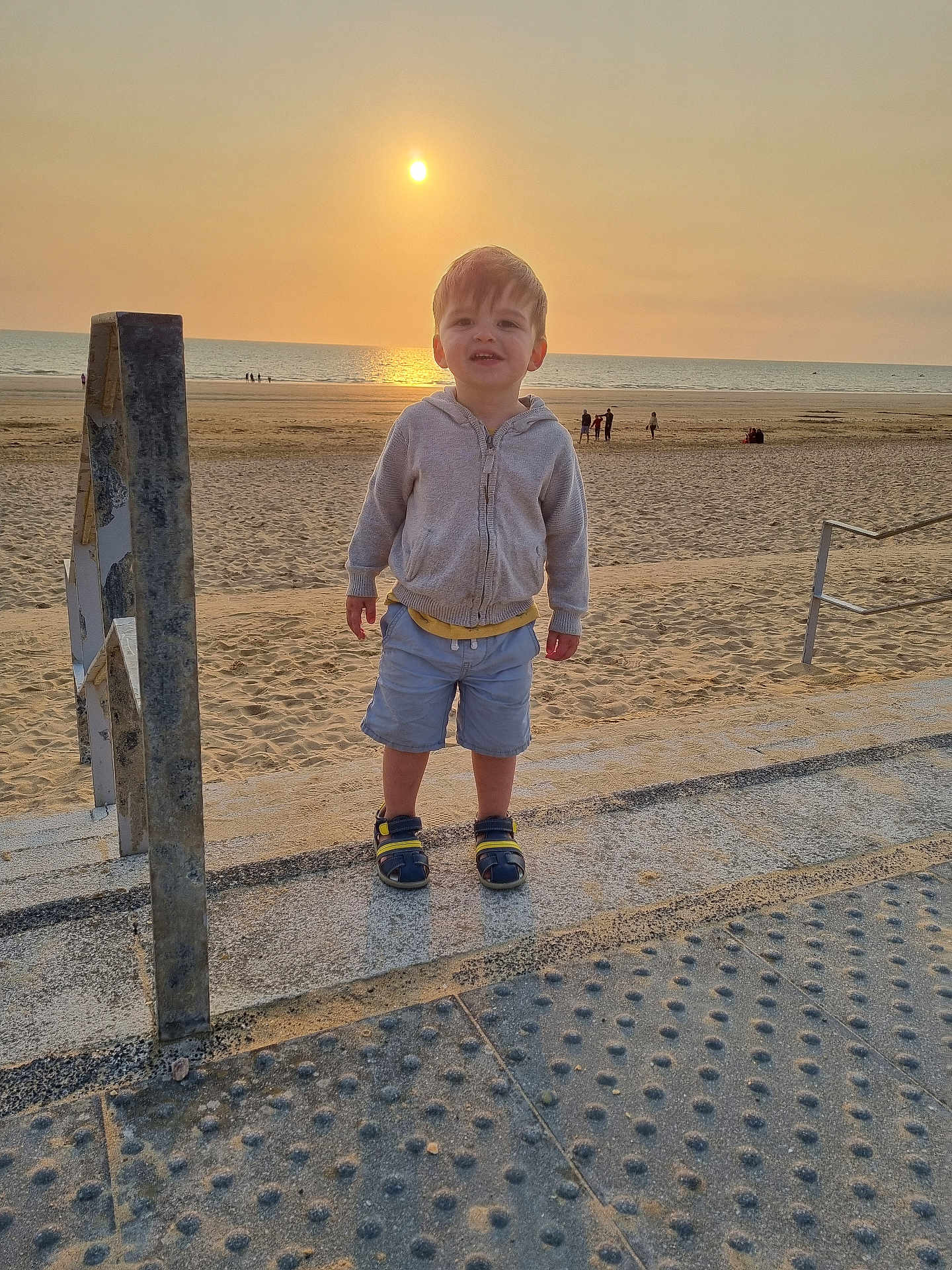 Sacha participe au concours pour gagner de l'argent avec cette photo : toddler, child, beach, sunset, sand, sea, ocean, clothing, hoodie, shorts, sandals, concrete, railing, outdoor, sky, sun, people, shadows, summer, vacation