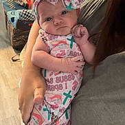 Madison joined the competition — help win amazing prizes! baby, infant, child, person, holding, headband, bow, clothing, patterned_outfit, indoor, adult_arm, floor, carpet, furniture, couch, wooden_chair, curious, portrait, closeup, home