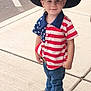 child, boy, cowboy_hat, american_flag_shirt, jeans, boots, sidewalk, outdoor, smiling, portrait, standing, cute, fashion, hat, person, clothing, concrete, street, young, casual