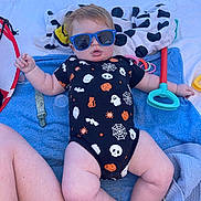 Mason joined the competition — help win amazing prizes! baby, sunglasses, onesie, halloween, toy_shovel, towel, outdoor, child, infant, legs, arm, plastic_toy, blue, black_clothing, white_towel, patterned_clothing, sunlight, relaxing, cute, playtime